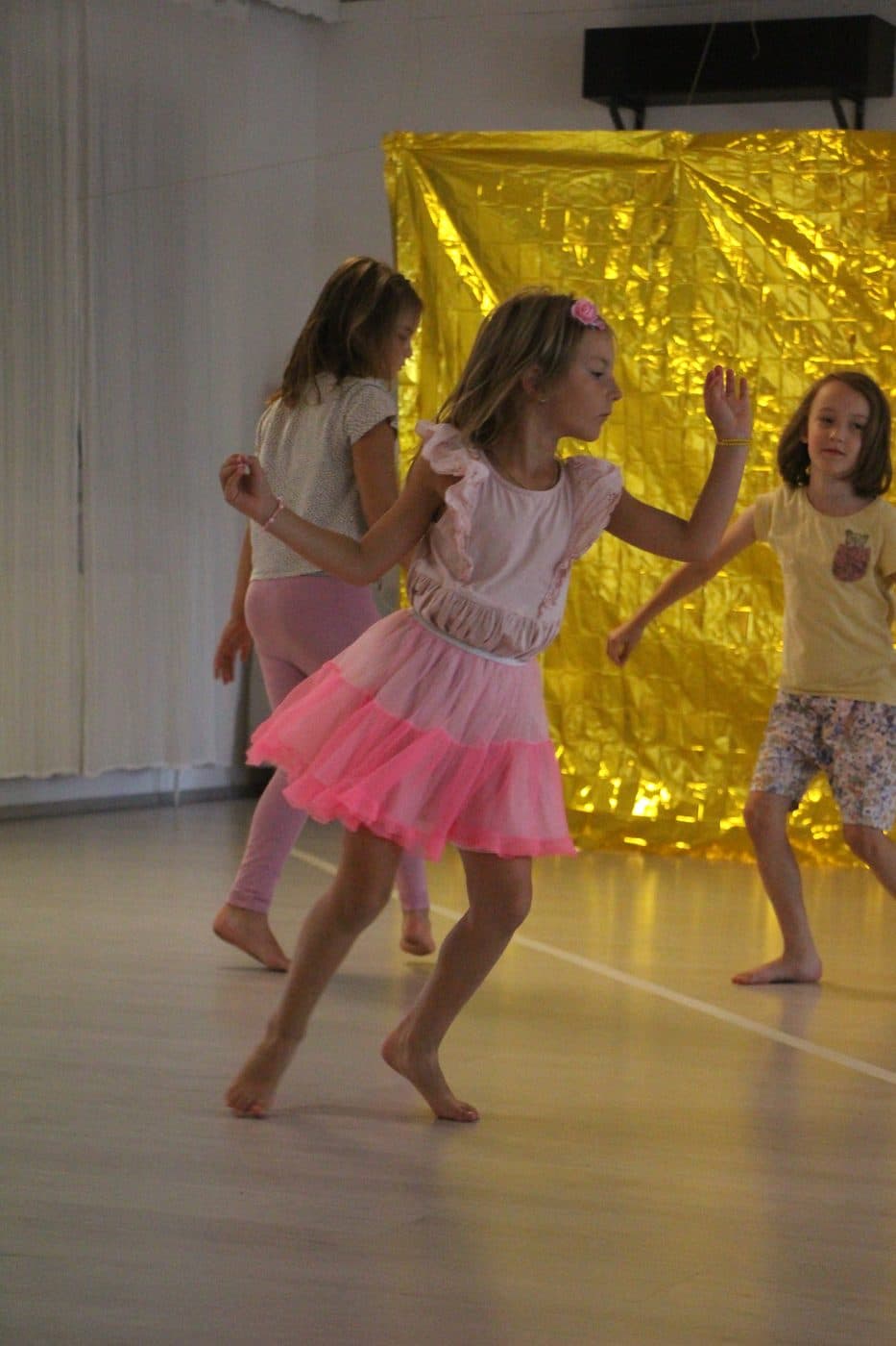 Drei Mädchen tanzen barfuß im Tanzsaal vor einem goldenen Vorhang